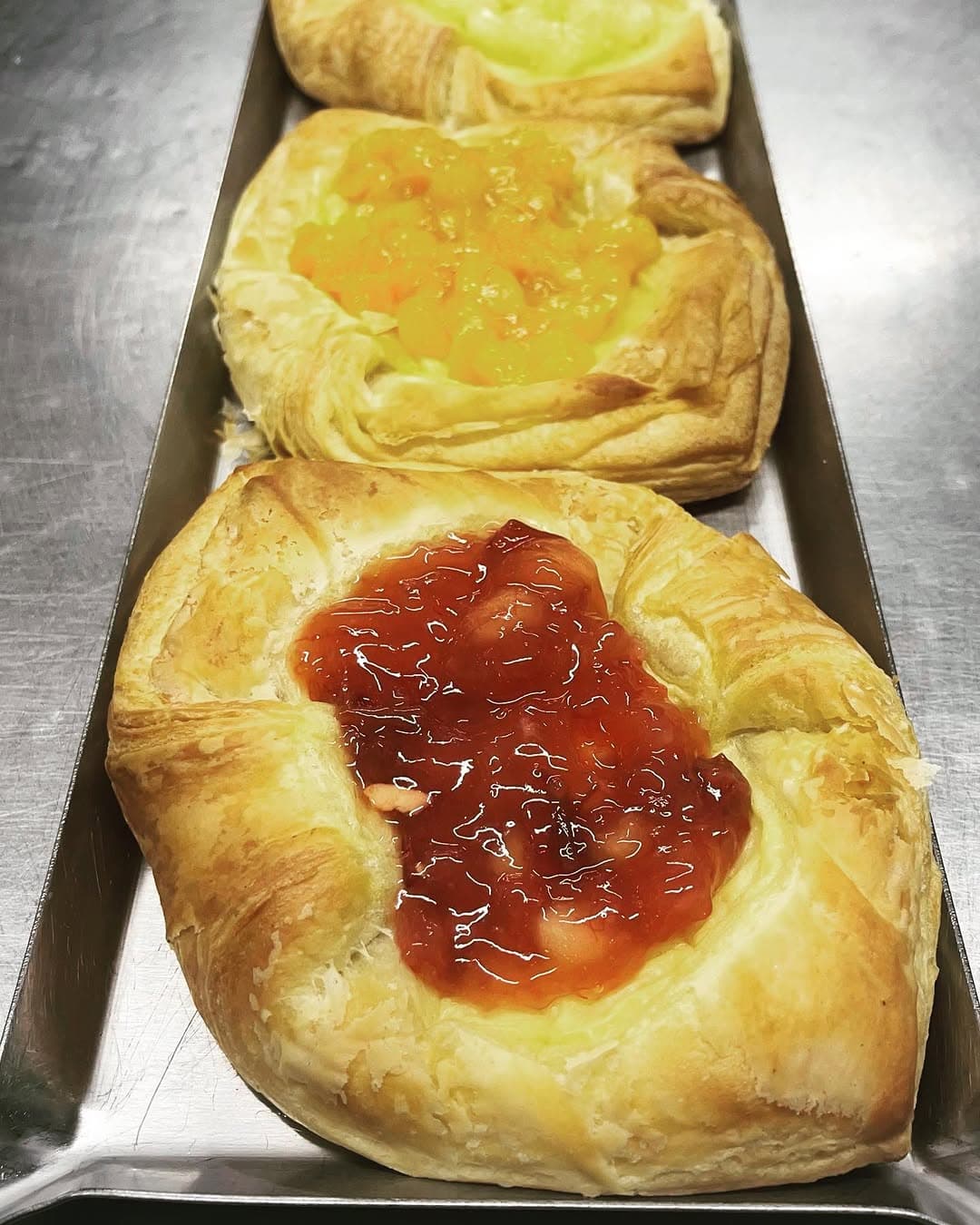 Fruit danishes with apricot, apple and berry filling on a bakery tray