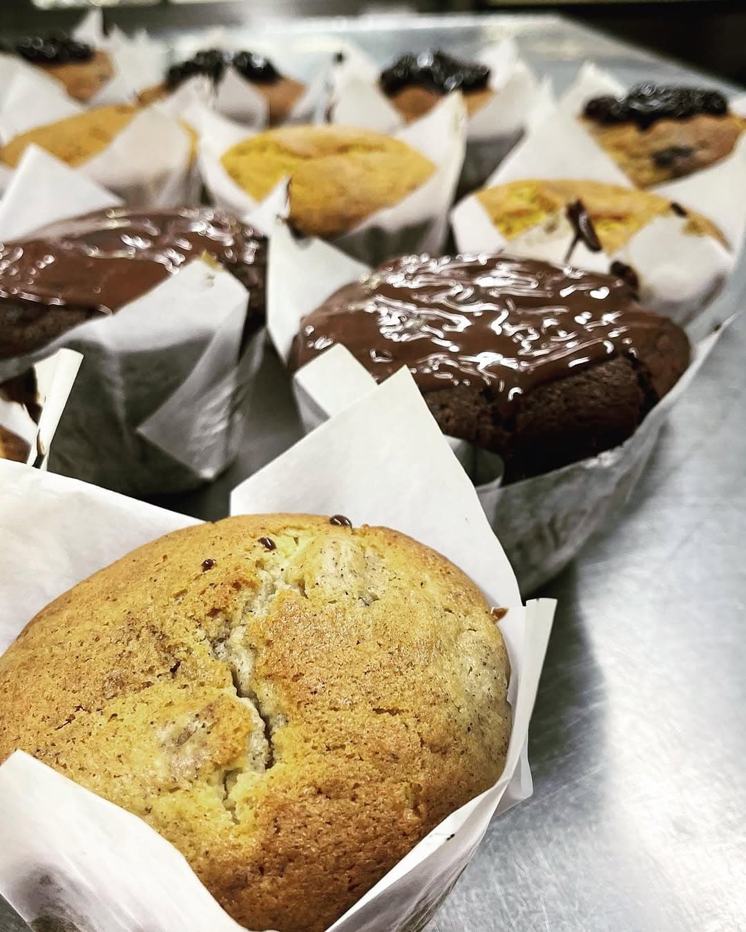 Chocolate-topped and plain muffins in paper wraps on a bakery tray
